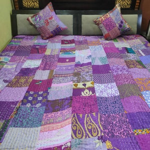 Op de afbeelding: Paarse kantha-deken met een patchwork-ontwerp. De deken is gemaakt van verschillende tinten paarse stof en is gestikt met een doorlopende steek. De deken wordt getoond op een bed met twee bijpassende kussenslopen.