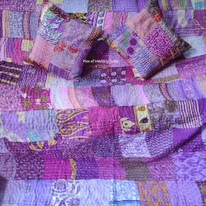 May include: Purple kantha quilt with a patchwork design. The quilt is made of various shades of purple and features intricate embroidery. Two matching purple throw pillows are included.