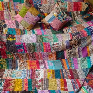 Peut inclure: Une courtepointe colorée en patchwork avec une variété de tissus et de motifs. La courtepointe est composée de carrés et de rectangles de différentes tailles et couleurs. La courtepointe est pliée en deux et a deux oreillers sur le dessus. Les oreillers sont également en tissu patchwork et présentent une variété de couleurs et de motifs. Le texte "Pieces of Mystery India" est visible sur l'un des oreillers.