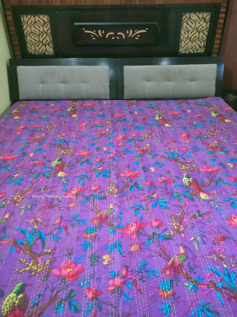 May include: Purple kantha quilt with a floral and bird pattern. The quilt is hand-stitched with yellow thread and features a variety of colors, including pink, green, and blue.