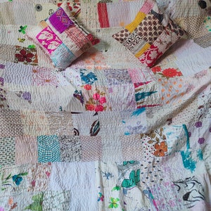 May include: A white kantha quilt with a patchwork design featuring various floral and geometric patterns in shades of pink, blue, brown, and green. The quilt is made of recycled saris and has a hand-stitched design. Two matching pillow covers are included.