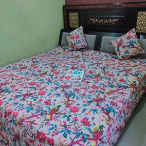 May include: A white bed with a floral patterned duvet cover. The duvet cover features a variety of colorful flowers and birds. The bed has a black headboard with a decorative design. A book with the letters "ABC" is on the bed.