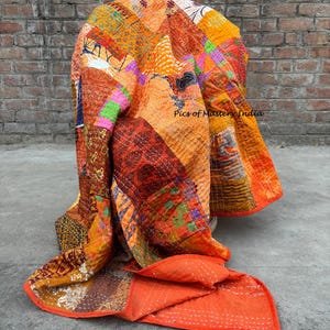 May include: A patchwork quilt in shades of orange, red, and brown, draped over a chair. The quilt features a variety of patterned fabrics and visible stitching. The text "Pics of Mastery India" is visible on the quilt.