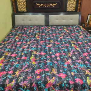 May include: A black kantha quilt with a floral and bird pattern. The quilt is made of cotton and has a hand-stitched design. The quilt is on a bed with a wooden headboard.