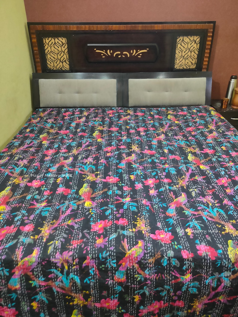 May include: A black kantha quilt with a floral and bird pattern. The quilt is made of cotton and has a hand-stitched design. The quilt is on a bed with a wooden headboard.