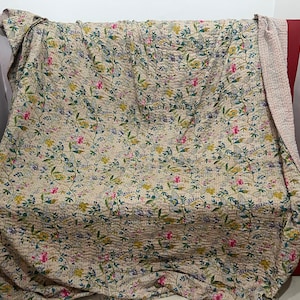 Könnte beinhalten: Beige Blumendecke mit einem sich wiederholenden Muster aus Blumen und Blättern in Rosa, Gelb, Blau und Grün. Die Decke ist über einen roten Stuhl drapiert und hat eine kontrastierende beige Rückseite.