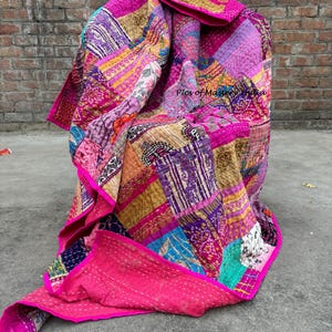 May include: A vibrant patchwork quilt in shades of pink, purple, gold, and blue. The quilt is made of various fabric pieces stitched together, with a bright pink border. The text "Pics of Mastery India" is visible in the image.