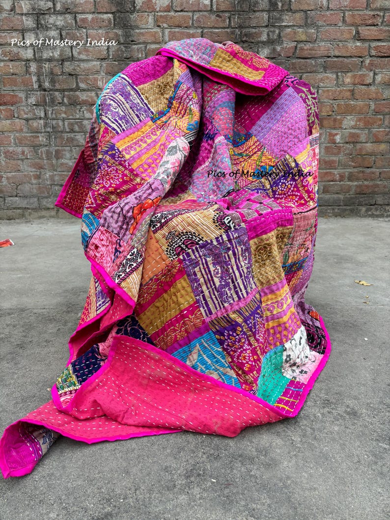 May include: A vibrant patchwork quilt in shades of pink, purple, gold, and blue. The quilt is made of various fabric pieces stitched together, with a bright pink border. The text "Pics of Mastery India" is visible in the image.
