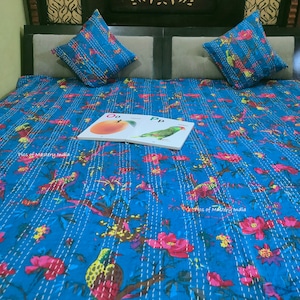 May include: A blue kantha quilt with a floral and bird pattern. The quilt is on a bed with two pillows. A children's book with the letters "Oo" and "Pp" is on the quilt.