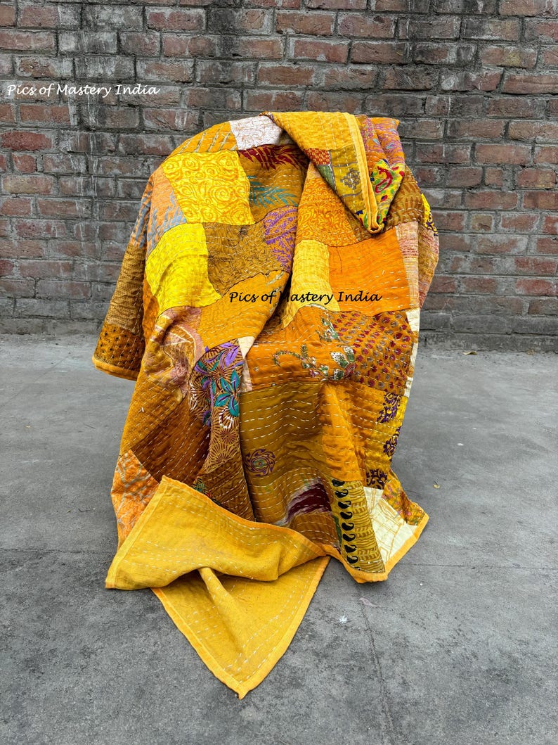 May include: A patchwork quilt in shades of yellow, orange, and brown, draped over a chair. The quilt features a variety of patterns and textures, with visible stitching. The words "Pics of Mastery India" are visible on the quilt.