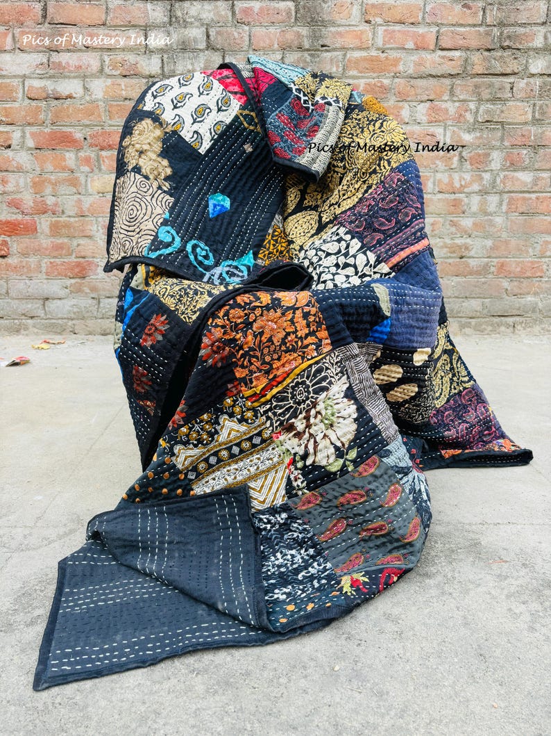 May include: A patchwork quilt with a variety of patterned fabric squares in shades of black, blue, red, orange, and gold. The quilt is folded, revealing the intricate stitching and the reverse side of the quilt. The text "Pics of Mastery India" is visible.