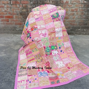 May include: A pink patchwork quilt featuring a variety of embroidered fabric squares in shades of pink, gold, white, and green. The textile displays intricate floral and geometric patterns with metallic thread accents and a solid pink border. Text reads Pics Of Mastery India.