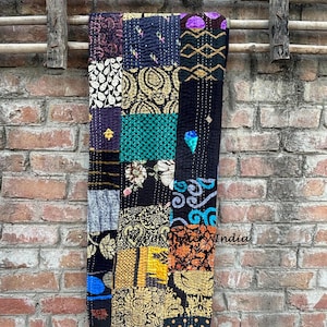 Peut inclure: Une courtepointe patchwork avec une variété de carrés à motifs en noir, or, sarcelle et violet. La courtepointe est suspendue contre un mur de briques et une structure en bois. La courtepointe est faite de divers tissus et cousue ensemble.