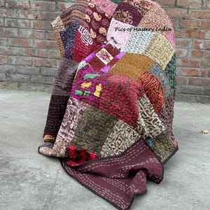 May include: A patchwork quilt draped over a chair, featuring a variety of fabrics in shades of burgundy, pink, brown, and green. The quilt has a stitched design and the text "Pics of Mastery India" is visible.