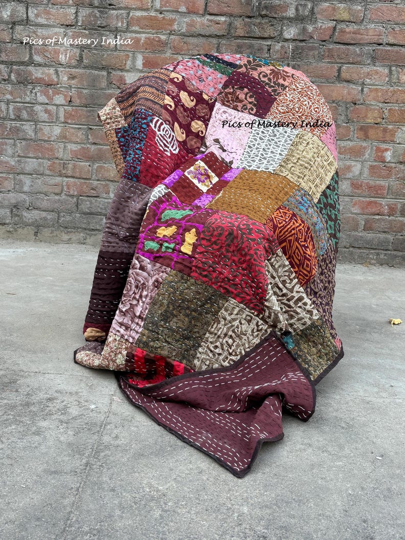 May include: A patchwork quilt draped over a chair, featuring a variety of fabrics in shades of burgundy, pink, brown, and green. The quilt has a stitched design and the text "Pics of Mastery India" is visible.