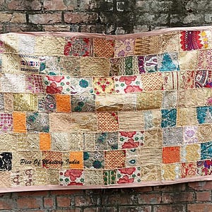 Puede incluir: Un tapiz rectangular de patchwork que presenta una variedad de cuadrados de tela bordados en tonos dorados, rojos, naranjas, azules y verdes. El textil incluye intrincados patrones florales y geométricos con detalles de hilo metálico y el texto Pics Of Mastery India.