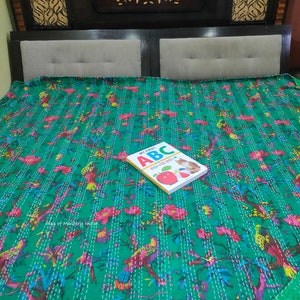 May include: A green kantha quilt with a floral and bird print. The quilt is on a bed with a brown headboard. A children's book titled "My First ABC Board Book" is on top of the quilt.