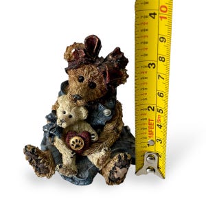 May include: A brown bear figurine holding a smaller cream-coloured bear, both wearing denim overalls. The bears are seated, with a heart-shaped emblem. The figurine measures approximately 7.6 cm tall.