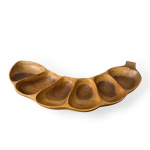 May include: A wooden serving tray with six curved compartments. The tray is made of a light brown wood with darker wood grain patterns. The tray has a handle on one end and is designed for serving snacks or appetizers.