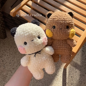Op de afbeelding: Twee knuffels van getextureerd garen, &eacute;&eacute;n wit met zwarte oren en roze wangen, de andere bruin met zwarte oren en gele wangen. Beide hebben zwarte ogen en een kleine mond. De tekst ig: shine.crafts is zichtbaar in de linkerbovenhoek.