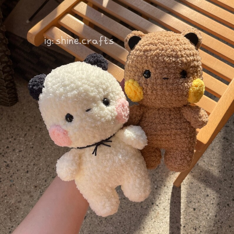 Op de afbeelding: Twee knuffels van getextureerd garen, &eacute;&eacute;n wit met zwarte oren en roze wangen, de andere bruin met zwarte oren en gele wangen. Beide hebben zwarte ogen en een kleine mond. De tekst ig: shine.crafts is zichtbaar in de linkerbovenhoek.