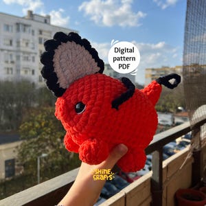 Könnte beinhalten: Ein handgefertigtes, rotes Häkeltier mit schwarzen und grauen Akzenten. Das Spielzeug hat einen stacheligen Rücken und einen kleinen Schwanz. Der Text "Digital pattern PDF" ist sichtbar. Das Spielzeug wird in einer Hand gehalten.