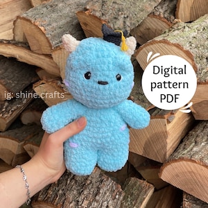 May include: A light blue crocheted monster toy wearing a black and yellow graduation cap. The toy is sitting on a pile of wood logs. The text "Digital pattern PDF" is written on the image.