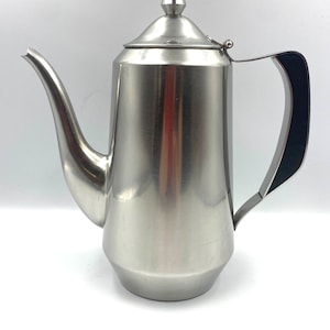 Könnte beinhalten: Eine silberne Teekanne aus Edelstahl mit schwarzem Griff und einem spitzen Deckel.