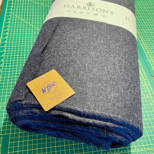 Puede incluir: Un rollo de tela Harrisons gris oscuro con una etiqueta blanca que dice "HARRISONS" y una etiqueta marr&oacute;n que dice "W. BILL SINCE 1918".
