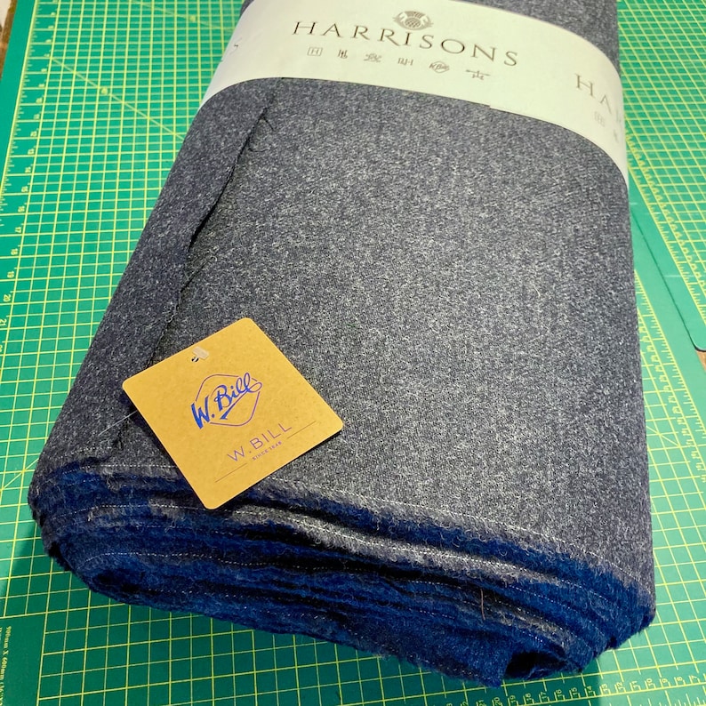 Puede incluir: Un rollo de tela Harrisons gris oscuro con una etiqueta blanca que dice "HARRISONS" y una etiqueta marr&oacute;n que dice "W. BILL SINCE 1918".