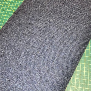 Puede incluir: Primer plano de una tela vaquera azul oscuro con un tejido texturizado. La tela est&aacute; sobre una estera de corte verde.