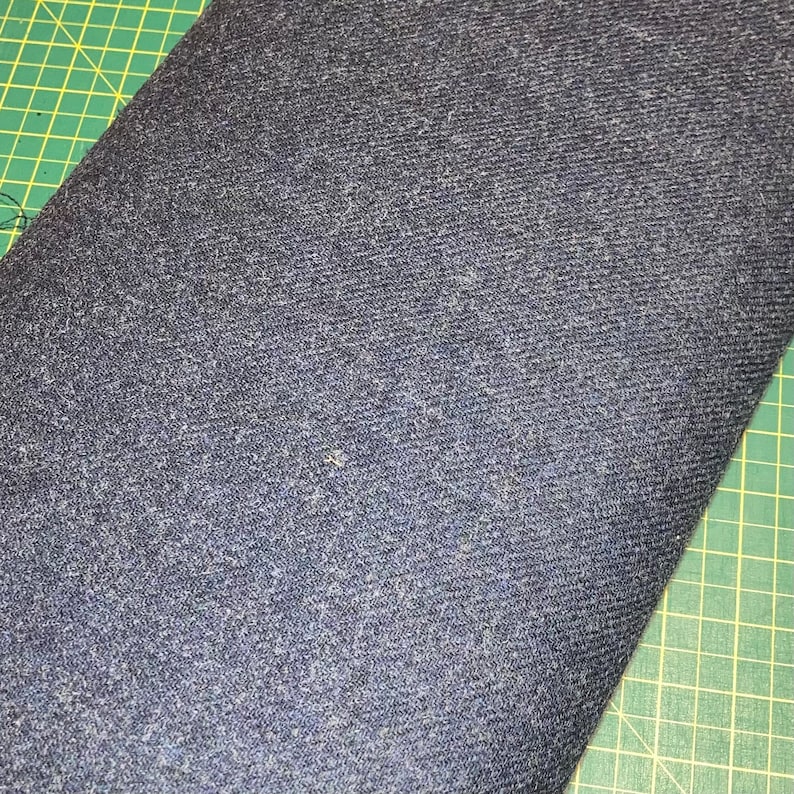 Puede incluir: Primer plano de una tela vaquera azul oscuro con un tejido texturizado. La tela est&aacute; sobre una estera de corte verde.