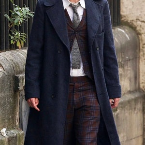 Puede incluir: Un hombre con un abrigo azul oscuro de doble botonadura sobre un chaleco a cuadros y una corbata estampada. Lleva una camisa blanca y pantalones a cuadros.