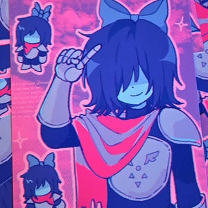 May include: A colourful print depicting a cartoon character with dark blue hair, a red scarf, and a bow. The character is making a peace sign. The background is pink with stars and clouds. Smaller character images are also present.