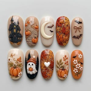 May include: A set of ten press-on nails featuring autumn and Halloween designs. The nails display motifs including a haunted house, pumpkins on a path, a crescent moon with bats, fall leaves, a ghost in a beanie, a white heart, and flowers.