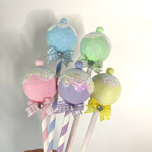 May include: Five pastel-colored, sparkly, round ornaments on sticks with striped paper straws and small bows. The ornaments are light blue, green, pink, purple, and yellow.