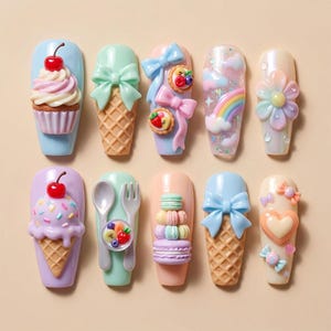 May include: A collection of ten artificial nails with various designs. The designs include a cupcake, ice cream cone, bow, rainbow, flower, spoon and fork with fruit, and macarons. The nails are painted in pastel colors with decorative elements.