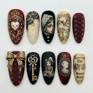May include: A collection of ten intricately designed artificial nails. Each nail features unique gothic-inspired art, including lace, portraits, musical notes, and decorative elements in shades of red, black, gold, and cream. The designs showcase a variety of textures and embellishments.