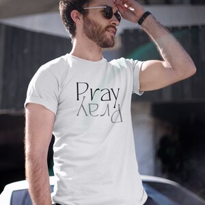 以下が含まれることがあります： 前面に黒で「Pray」という文字がプリントされた白いTシャツで、その下に「Pray」という文字が鏡文字でプリントされています。
