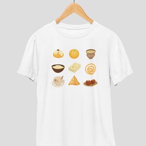 Op de afbeelding: Wit T-shirt met een afbeelding van negen verschillende Indiase zoetigheden en snacks, waaronder een kom kheer, een bord gulab jamun en een kopje chai.