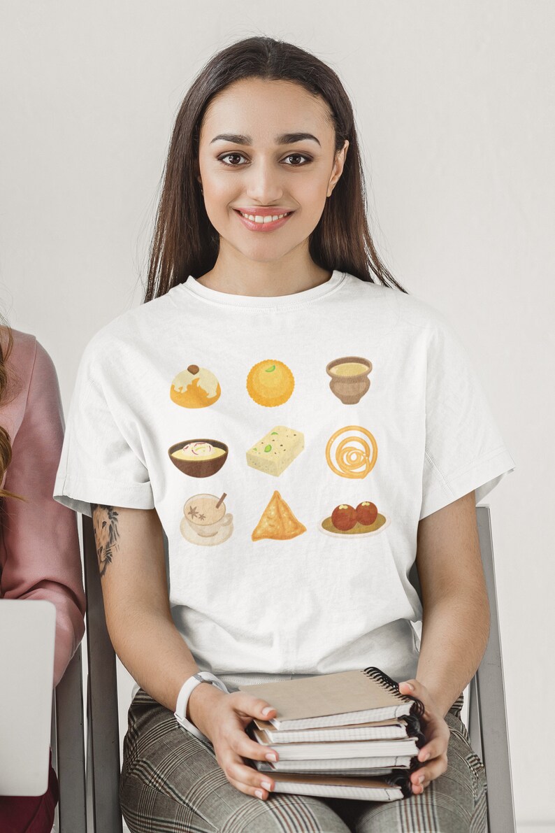 Op de afbeelding: Een wit T-shirt met een grafische print van negen verschillende Indiase zoetigheden en snacks. De afbeelding bevat een kopje chai, samosa's, jalebi, ladoo, gulab jamun en meer.