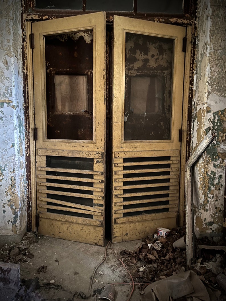 Puede incluir: Un par de puertas de madera amarilla desgastadas con una pantalla y un fondo de listones. Las puertas est&aacute;n ligeramente entreabiertas y est&aacute;n colocadas en una pared de ladrillo en ruinas.