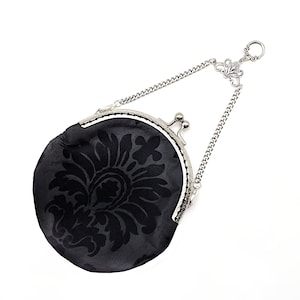 K&ouml;nnte beinhalten: Eine schwarze Stoffm&uuml;nzb&ouml;rse mit einer silbernen Kette und einem Verschluss. Die B&ouml;rse hat ein Blumenmuster.
