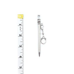 May include: A silver-toned mechanical pencil with a ribbed top section and a dangling charm attached by a lobster clasp. A white measuring tape is positioned alongside the pencil, indicating a length of approximately 4.5 inches.