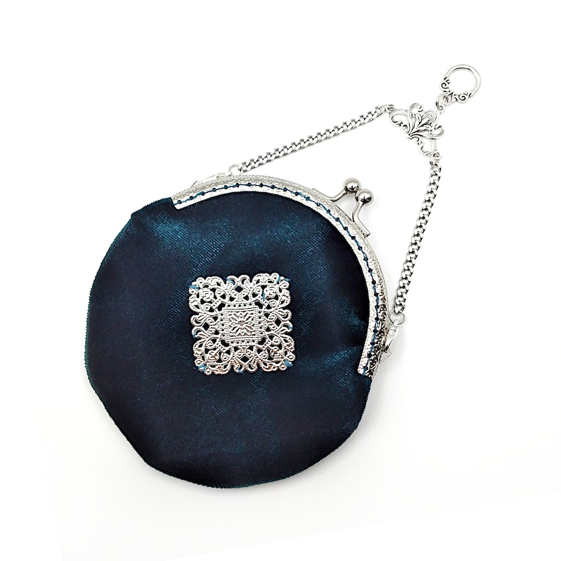 K&ouml;nnte beinhalten: Eine tealblaue Samt-M&uuml;nzb&ouml;rse mit einer silbernen Kette und einem silbernen Filigranmuster auf der Vorderseite.