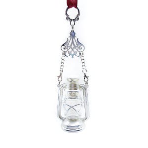 May include: A silver hanging oil lamp with a clear glass container and a decorative metal top. The lamp is suspended from a chain and has a red ribbon attached to the top.