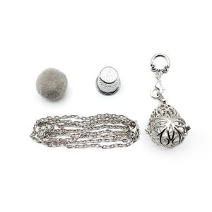 May include: A silver chain necklace with a silver cage pendant and a silver thimble. A gray felt ball is also included.