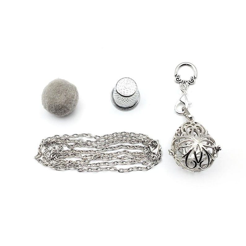 May include: A silver chain necklace with a silver cage pendant and a silver thimble. A gray felt ball is also included.