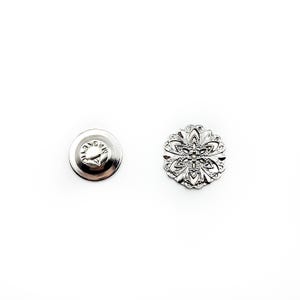 May include: A silver-toned metal button with a decorative floral design. The button has a flat back with a small pin.