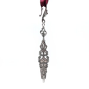 May include: Silver bookmark with an ornate design and a hook at the top. The bookmark is attached to a red ribbon.